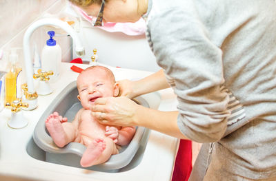 Babies crying while mother bathes in bathroom sink basin - newborn care