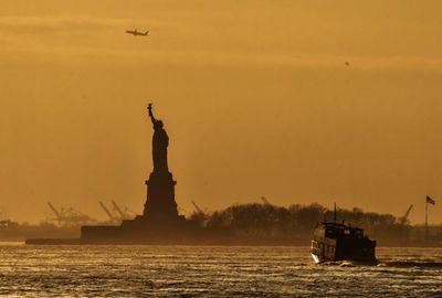 Statue in sea at sunset