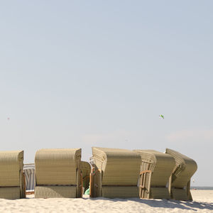 Hooded chairs on beach against clear sky