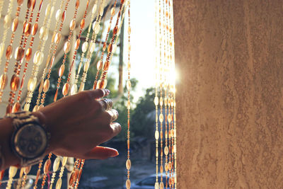 Hand of woman holding beaded curtain by wall