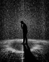 Silhouette man with umbrella walking on wet street