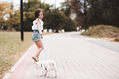 Funny baby girl 3-4 year old walking in park with puppy dog outdoors. summer time. childhood.