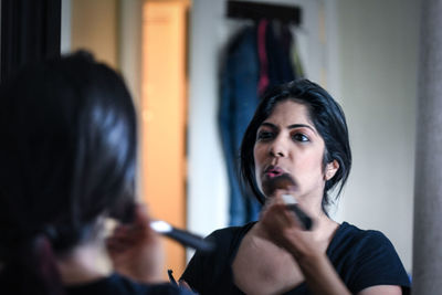 Reflection of woman applying blusher on face in mirror at home