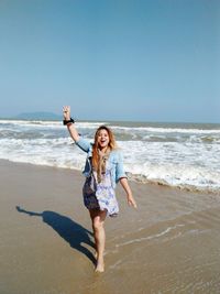 Happy young woman jumping on beach against clear sky