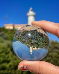 Cropped hand holding crystal ball against blue sky