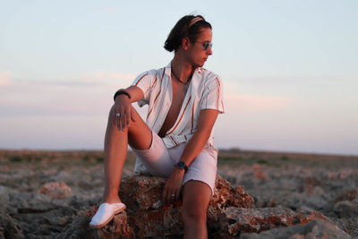 Handsome young man dressed in vintage clothes sitting on a desert rock at sunset in spain