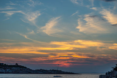 Isolated sailboat as the sun sets beyond clouds in the distance.