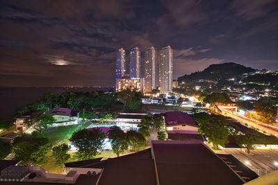 Illuminated buildings against cloudy sky at night