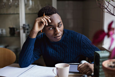 Thoughtful teenage boy looking away while doing homework at table