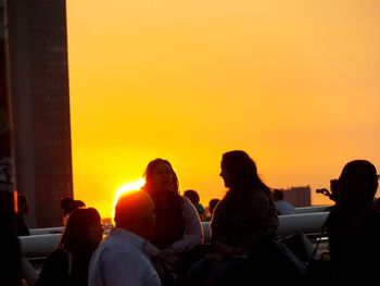 Silhouette people sitting against orange sky during sunset