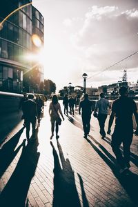 People walking on street in city against sky during sunset