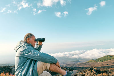 Rear view of man looking through binoculars at panoramic view of summits of active volcano etna