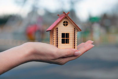 Close-up of hand holding small house against building