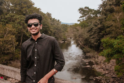 Portrait of young man standing against waterfall