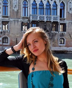 Thoughtful young woman sitting by grand canal against building
