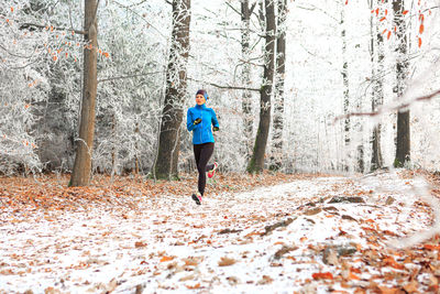 Full length of woman jogging in forest during winter