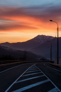 Road by mountains against sky during sunset