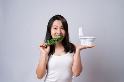 Portrait of young woman holding ice cream against white background