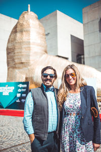 Portrait of smiling woman wearing sunglasses standing against built structure