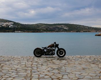 Motorcycle on footpath by lake against sky