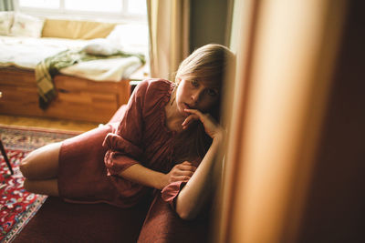 Young woman looking away while sitting on sofa at home