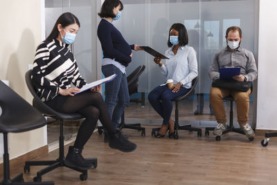 Interviewer reading resume while candidates sitting on chair at office