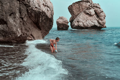 Shirtless boy holding squirt gun while standing in sea