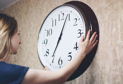 Side view of mid adult woman touching clock on wall