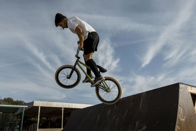 Young man jumping on ramp at bike park against sky