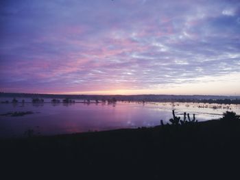 Silhouette people on lake against sky during sunset
