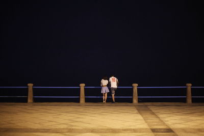 Rear view of couple standing by railing on promenade at night