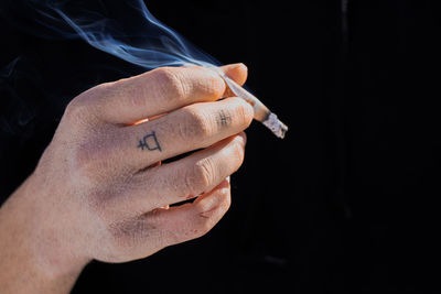 Cropped hand of man smoking cigarette against black background