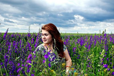 Beautiful young woman with flowers on field against sky