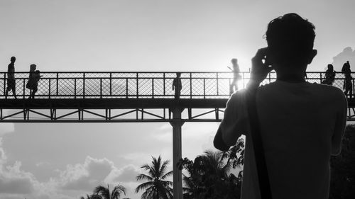 Rear view of silhouette man standing against bridge in city