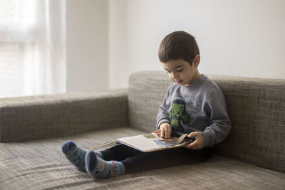 Full length of boy reading sitting on sofa
