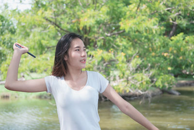 Happy young woman standing by tree against plants