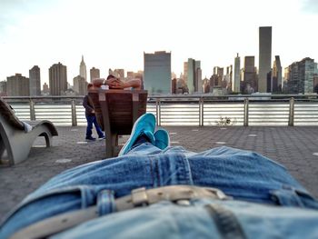 People sitting on sidewalk in city against sky