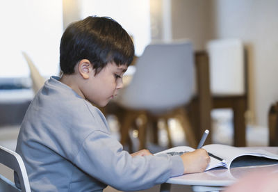 Side view of man writing in book at home