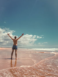 Rear view of man standing at beach against sky
