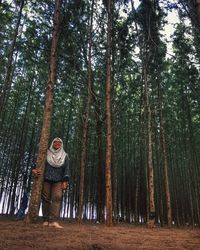 Full length of man standing by tree trunk in forest