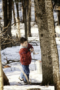 Boy making hole in tree trunk during winter