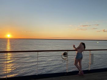 Man standing on railing against sea during sunset