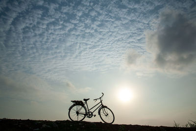 Silhouette person riding bicycle on field against sky during sunset