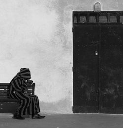 Person in robe sitting on bench against building