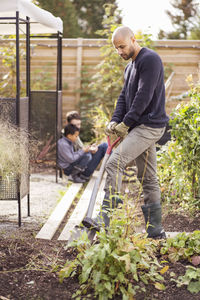 Man digging in garden with children in background