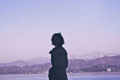 Rear view of woman standing by lake against clear sky