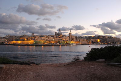 Illuminated buildings by sea against sky