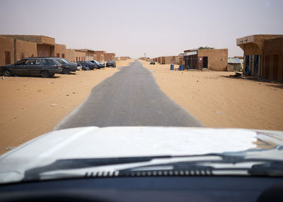 Car driving along asphalt road cutting through remote sandy town