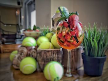 Close-up of chopped fruits in drinking glass by tennis balls on table