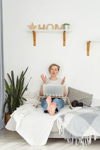 Woman using digital tablet while sitting on bed at home